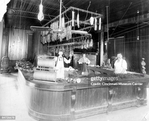 Interior of a local butcher shop with the butchers standing behind a counter, underneath the meats and produce that they sell, Cincinnati, ca.1920s.