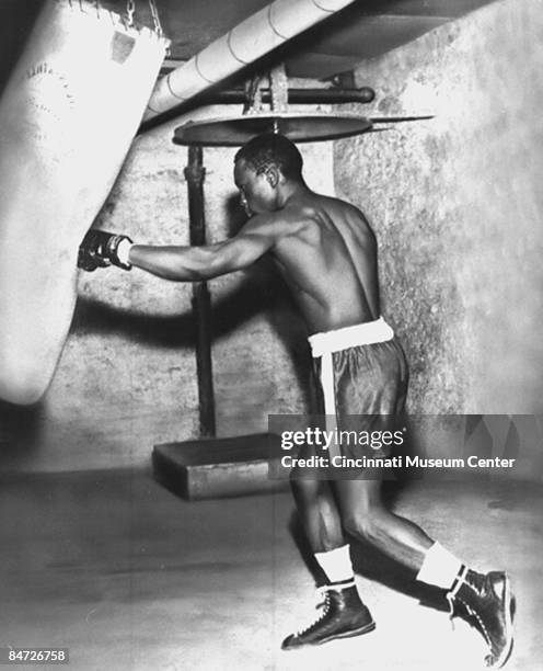 Heavyweight champion Ezzard Charles pounds away on the heavy bag while training for an unidentified fight, Cincinnati, ca 1950s.