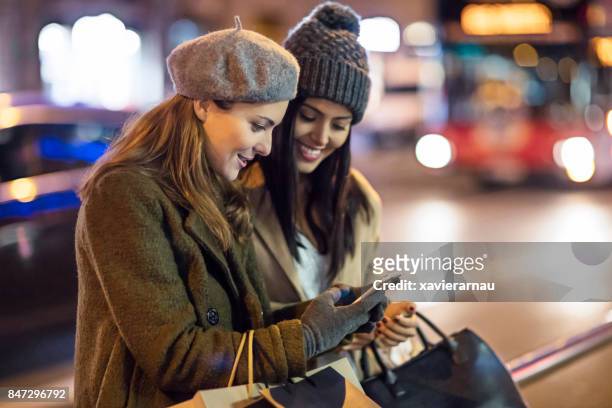 mooie vrouwen controleren van mobiele telefoon in de straat na het winkelen in de stad bij nacht - taxi españa stockfoto's en -beelden