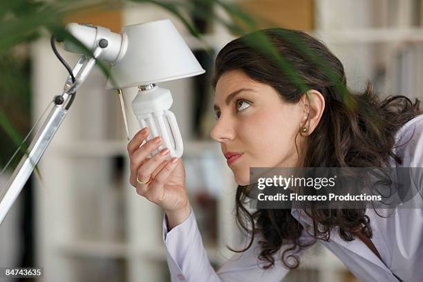 woman changing lightbulb - con eficaz consumo de energía fotografías e imágenes de stock