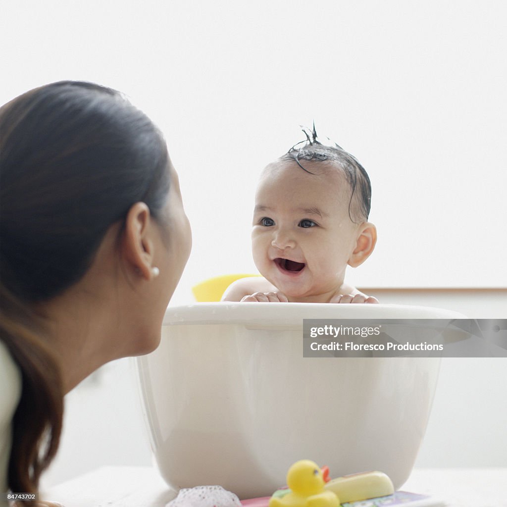 Baby girl in bathtub laughing at mother