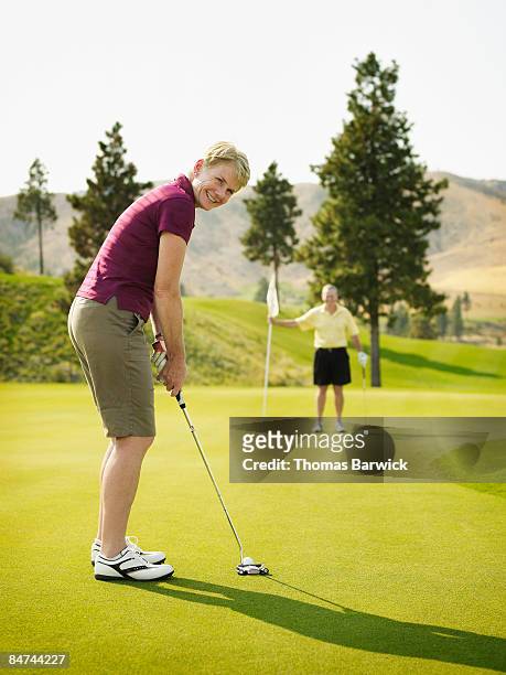 woman putting on green, man holding flag  - golf short iron stock pictures, royalty-free photos & images