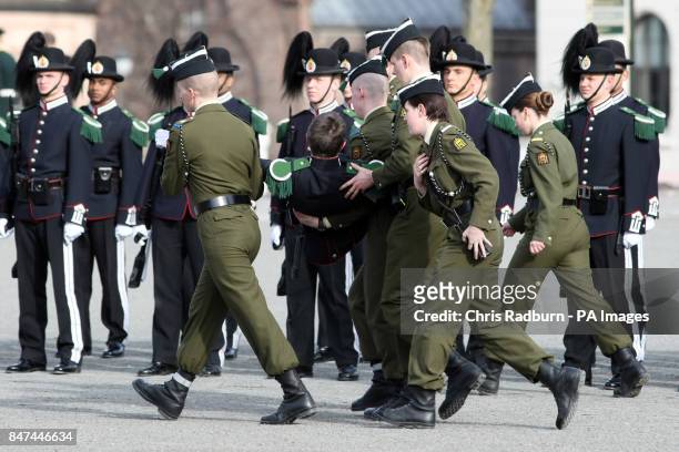 Serviceman is carried away after fainting in the Guard of Honor before the arrival of The Prince of Wales and The Duchess of Cornwall, at a wreath...