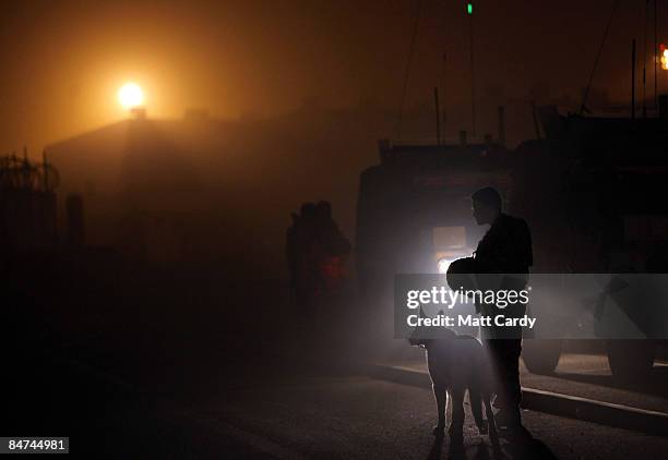 Dog handler and his dog wait as soldiers with 1 Logistic Support Regiment are briefed besides a Land Rover on the night convoy route they will be...