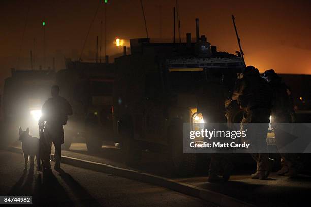 Dog handler and his dog wait as soldiers with 1 Logistic Support Regiment are briefed besides a Land Rover on the night convoy route they will be...