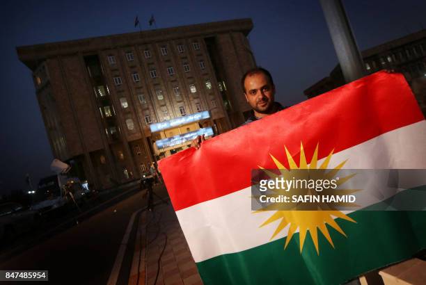 An Iraqi Kurdish man holds a Kurdish flag as he stands next to Kurdistan's parliament building in Arbil, the capital of the autonomous Kurdish region...