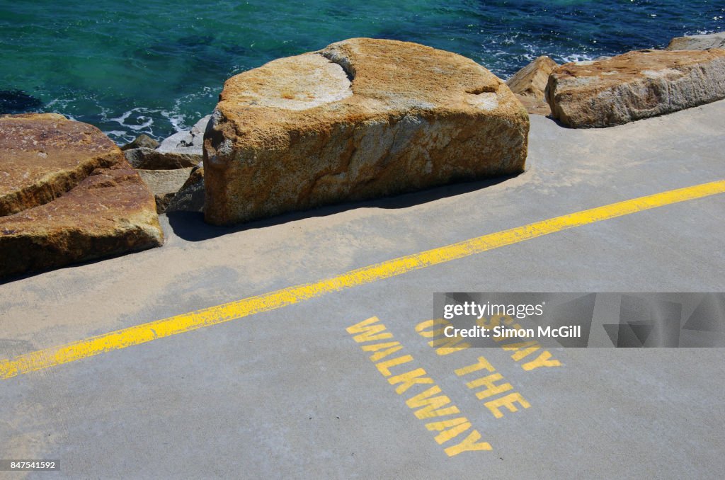 'Stay on the Walkway' sign stencilled in yellow paint on the concrete walkway of the Southern Break Wall at Coffs Harbour, New South Wales, Australia