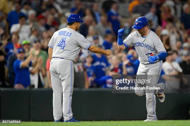 Third base coach Luis Rivera of the Toronto Blue Jays congratulates Justin Smoak on a solo home run against the Minnesota Twins as he runs the bases...