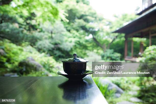 covered tea cup and saucer on table, japanese garden in background - chan stock pictures, royalty-free photos & images