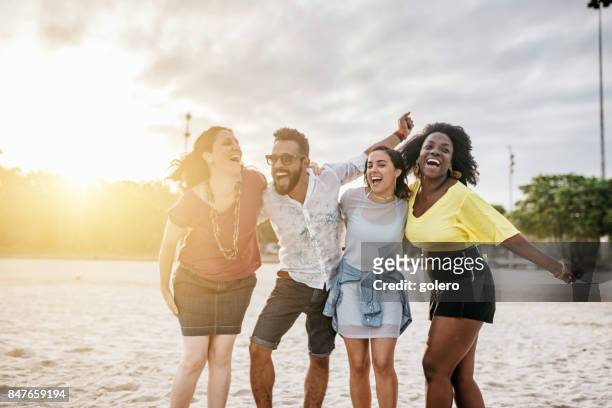 four happy brazilian friends embraced at beach at sunset hour - male with group of females stock pictures, royalty-free photos & images