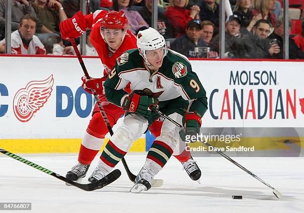 Mikko Koivu of the Minnesota Wild carries the puck past Jiri Hudler of the Detroit Red Wings with ice during their NHL game at Joe Louis Arena...