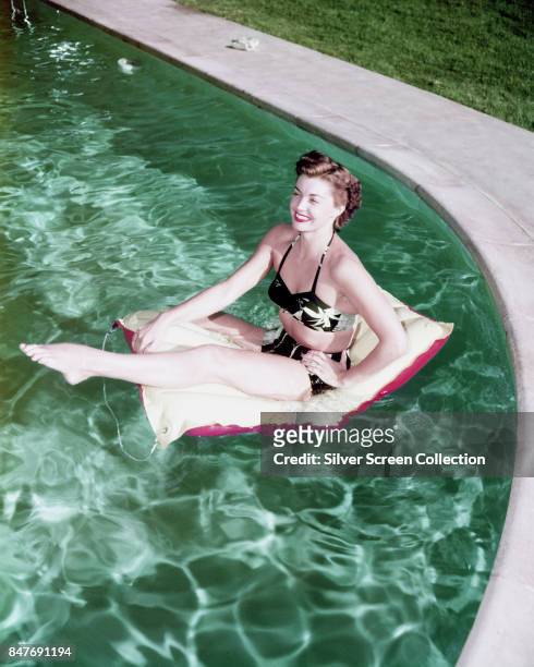 American competitive swimmer and actress Esther Williams sits on a inflatable float mat in a swimming pool, circa 1955.