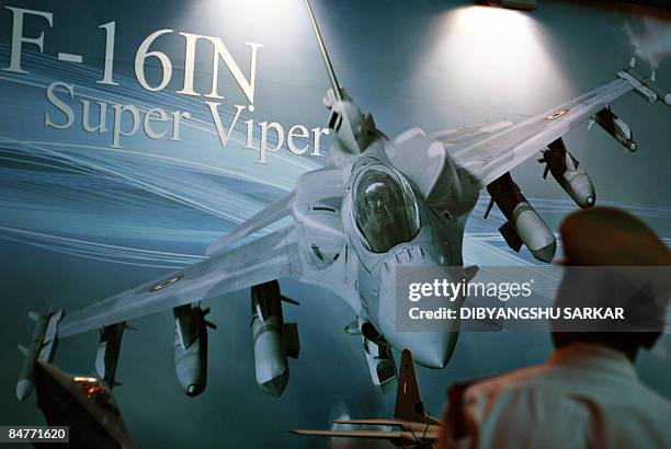 An Indian Police officer walks past a billboard at the Lockheed Martin booth depicting the F-16IN Super viper, based on the F-16F, proposed for the...