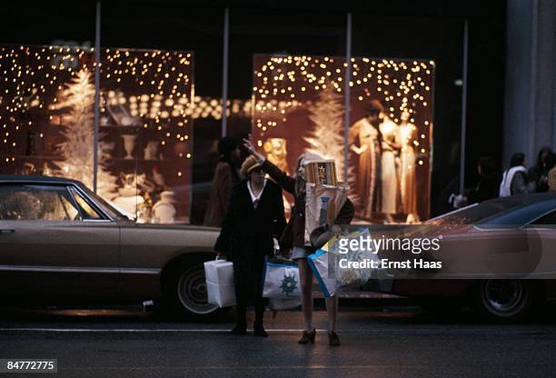 Heavily laden shopper hails a cab on Fifth Avenue, New York City, circa 1970.