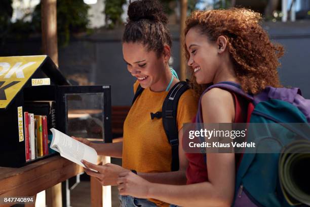 young women with backpacks smiling, while choosing books - choice student stockfoto's en -beelden