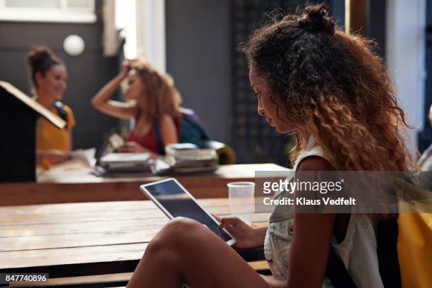 young woman reading on tablet, in courtyard of hostel - 3 teenagers mobile outdoors stock-fotos und bilder