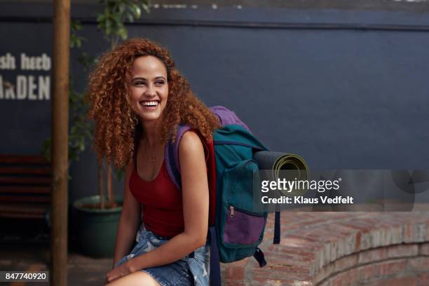young woman with backpack smiling, while sitting in courtyard - journey stock-fotos und bilder