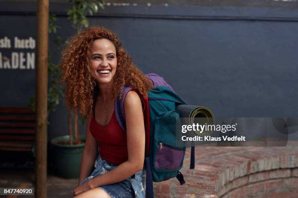 young woman with backpack smiling, while sitting in courtyard - tourist bildbanksfoton och bilder