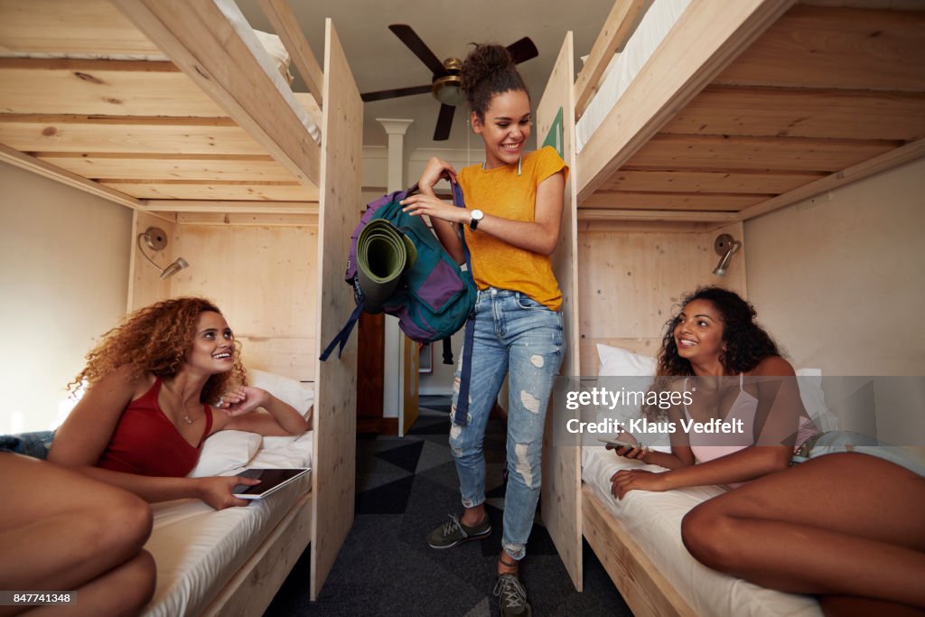 Young woman arriving at hostel room, two other women laying in bunk beds