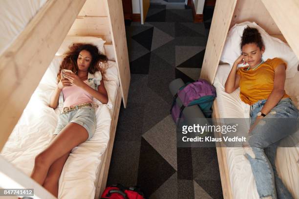 young woman checking phone in bunk bed, roommate sleeping in the other bed - hostel people travel stock-fotos und bilder