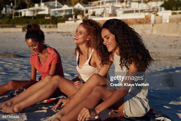 three young women sitting on beach and smiling - girls sunbathing stock pictures, royalty-free photos & images