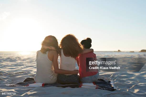 rear view of three young women sitting on beach - beste freunde teenager stock-fotos und bilder
