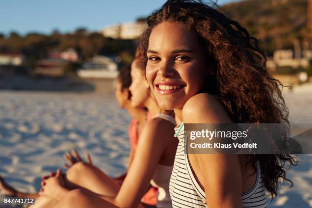 portrait of smiling young woman sitting on beach, with friends - girls sunbathing stock pictures, royalty-free photos & images