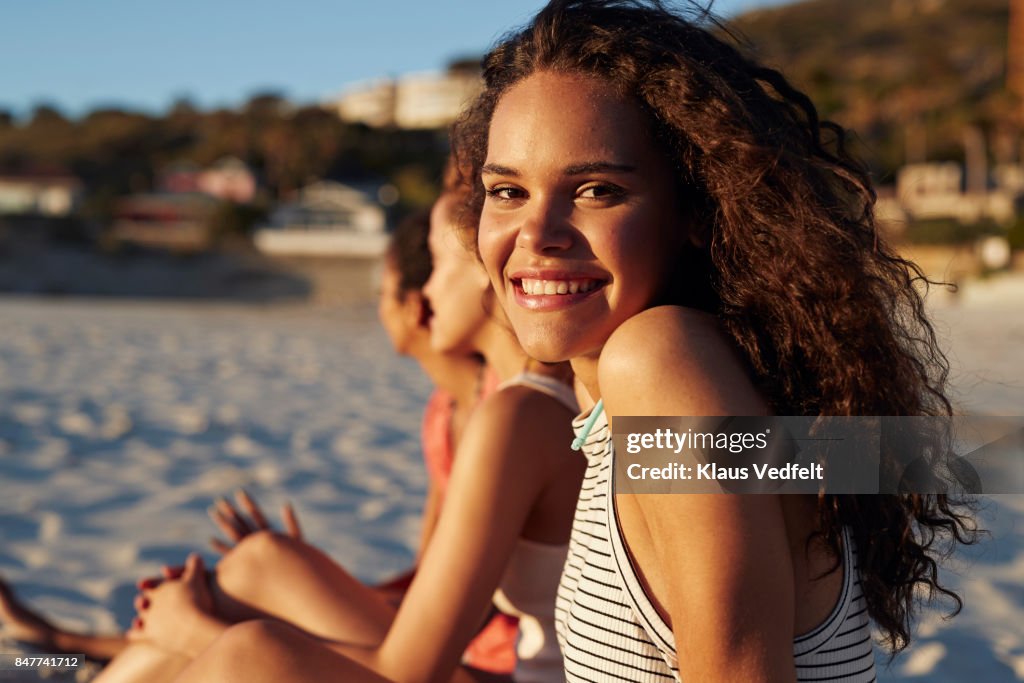 Portrait of smiling young woman sitting on beach, with friends
