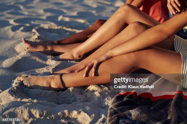 close-up of three young womens legs, on sandy beach - gebruind stockfoto's en -beelden