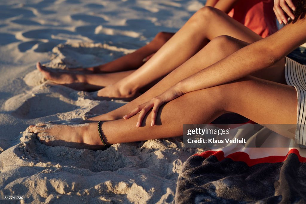 Close-up of three young womens legs, on sandy beach