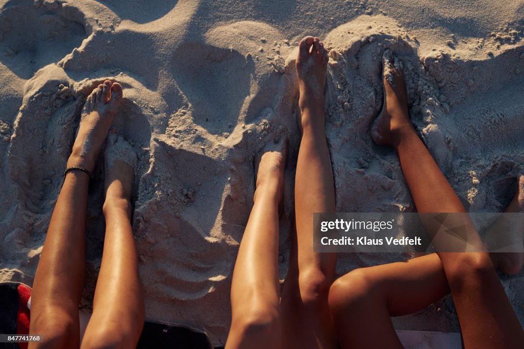 Close-up of three young womens legs, on sandy beach