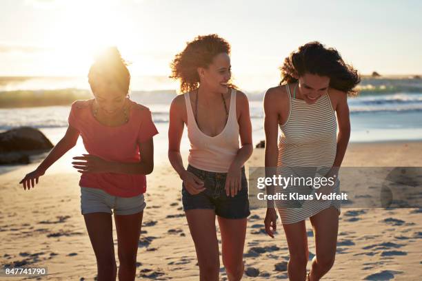 three young women walking together on sandy beach - girl beach sunset stock-fotos und bilder