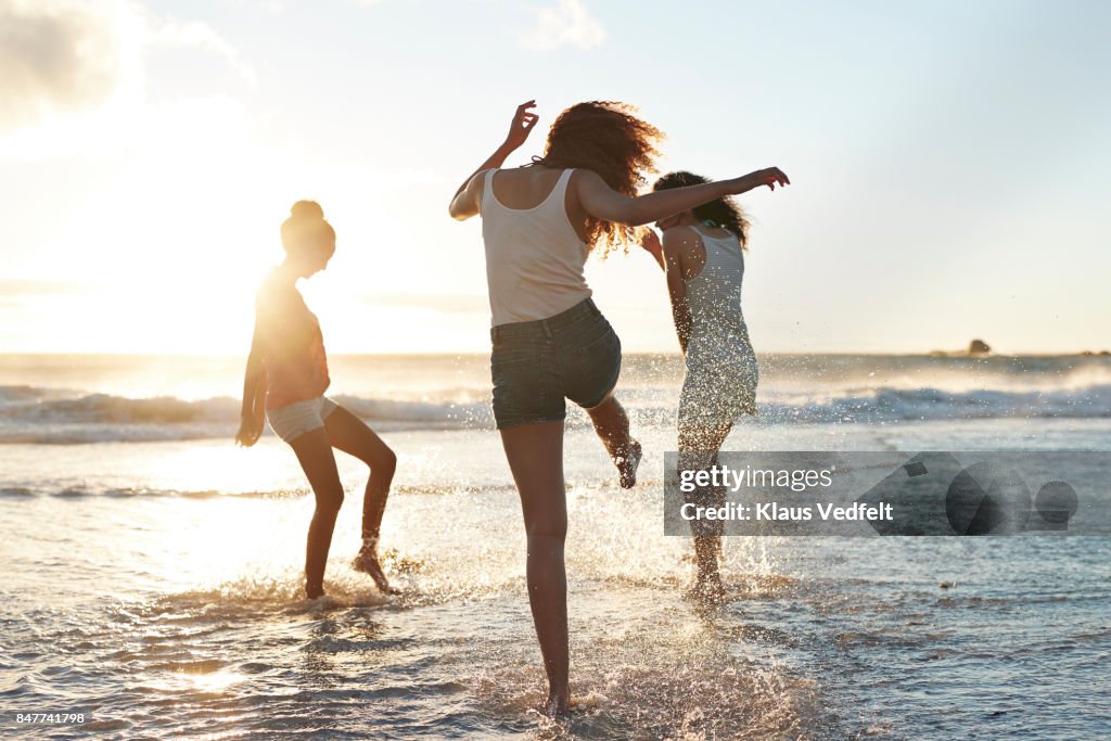 Three young women kicking water and laughing on the beach