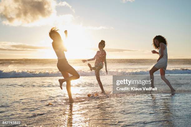 three young women kicking water and laughing on the beach - skinny teen ストックフォトと画像