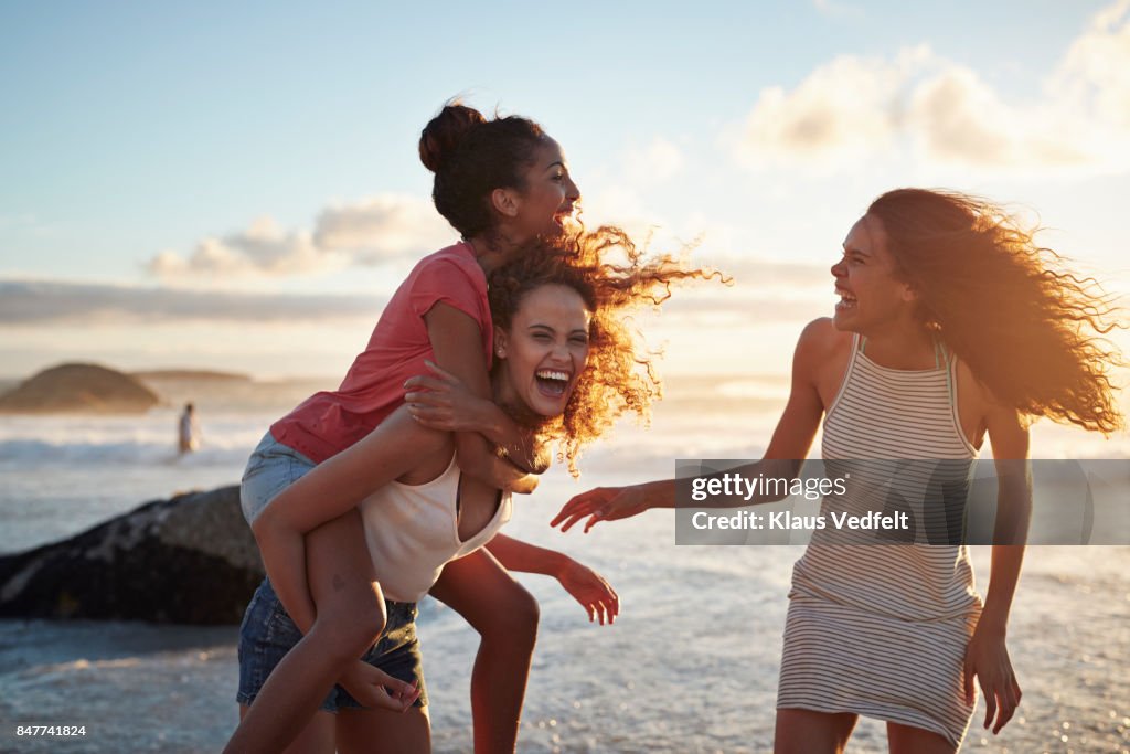 Young women piggybacking on sandy beach