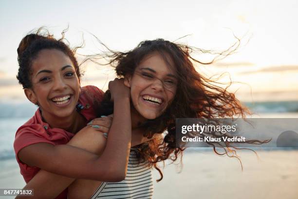 young women piggybacking on sandy beach - fonds marins foto e immagini stock