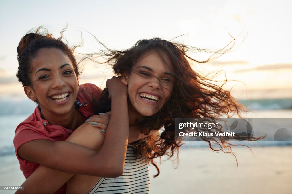 Young women piggybacking on sandy beach