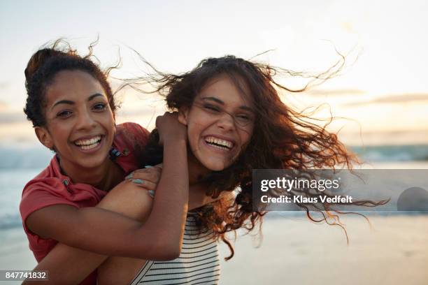 young women piggybacking on sandy beach - strand of human hair stock pictures, royalty-free photos & images