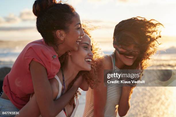 young women piggybacking on sandy beach - girl beach sunset stock-fotos und bilder