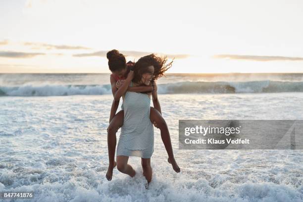 young women piggybacking in the water on beach - young teen girl beach ストックフォトと画像