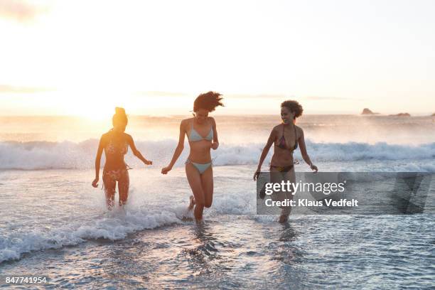 three young women running in the water, at the beach - fille maillot photos et images de collection