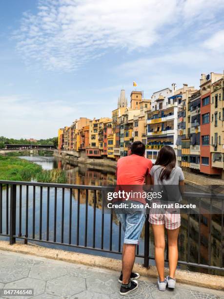 a pair of young women looking from on a bridge, cathedral and houses on onyar riverbank, spain, catalonia, girona. - rivière onyar photos et images de collection