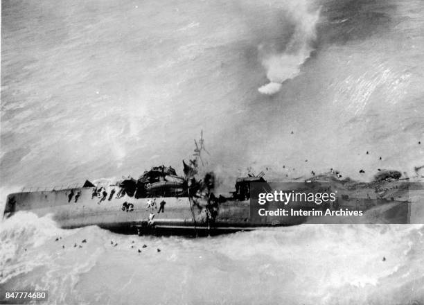 Aerial view of Japanese sailors both in the water and clinging to a sinking ship as it keels over after damage from a American B-25 bomber attack,...