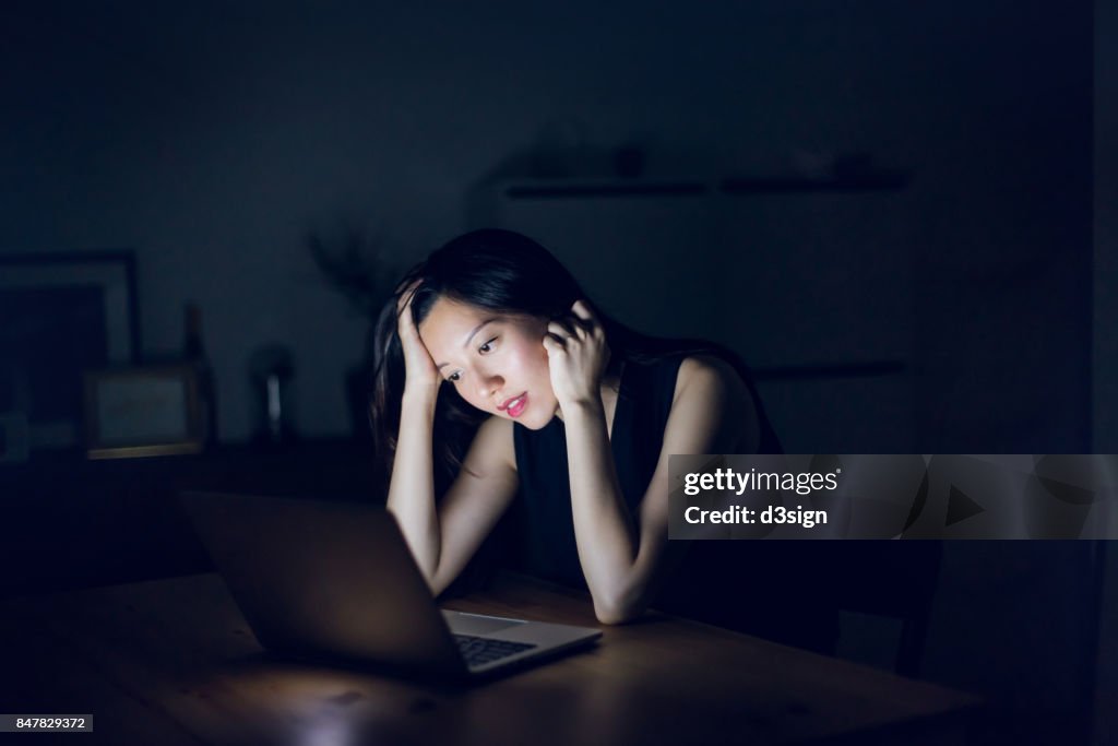 Stressed and frustrated businesswoman working on laptop till late at work