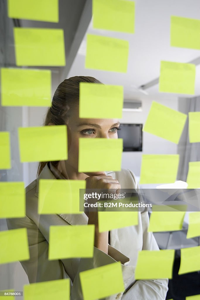 Businesswoman looking at sticky notes on window