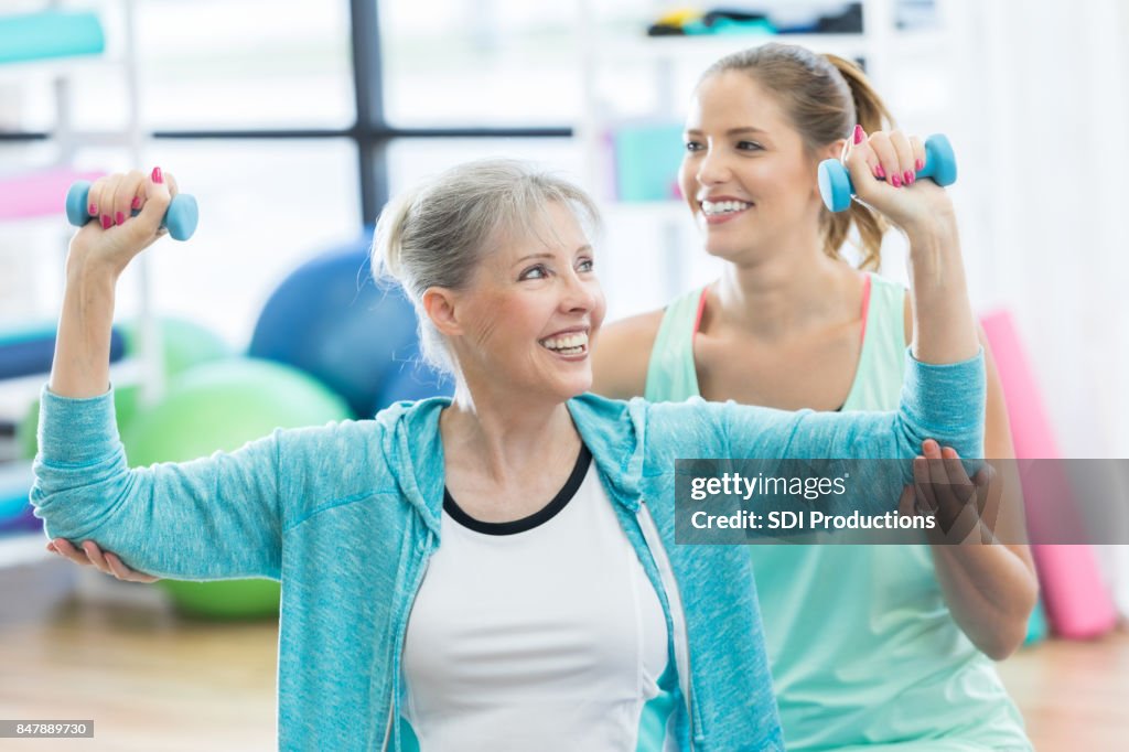 Cheerful senior woman enjoys weight training with fitness coach