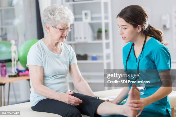 young doctor examines senior patient's leg - nurse legs stock pictures, royalty-free photos & images
