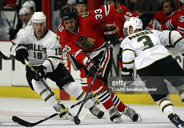 Dustin Byfuglien of the Chicago Blackhawks controls the puck under pressure from Stephane Robidas and James Neal of the Dallas Stars on February 14,...