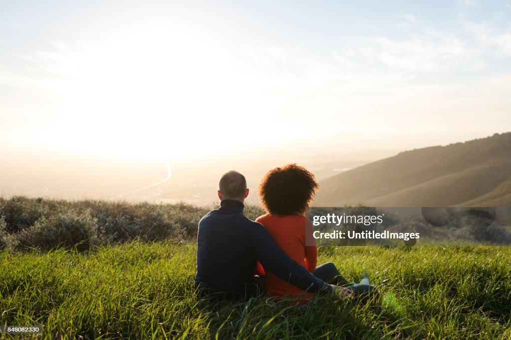 Couple sitting in a meadow and watching the sunset