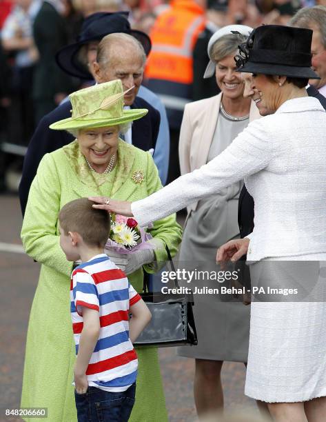 Queen Elizabeth II receives flowers from a young boy, watched by the Duke of Edinburgh, First Minister Peter Robinson and his wife Iris, in the...